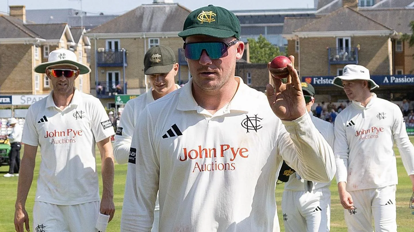 Liam Patterson-White holds up a red cricket ball with players surrounding him